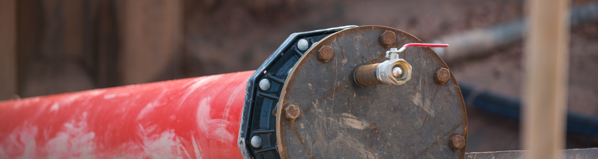 Red high-voltage cable duct with a bolted end plate and valve at a construction site.